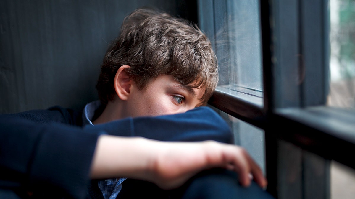 Sad teenaged boy looking out window.