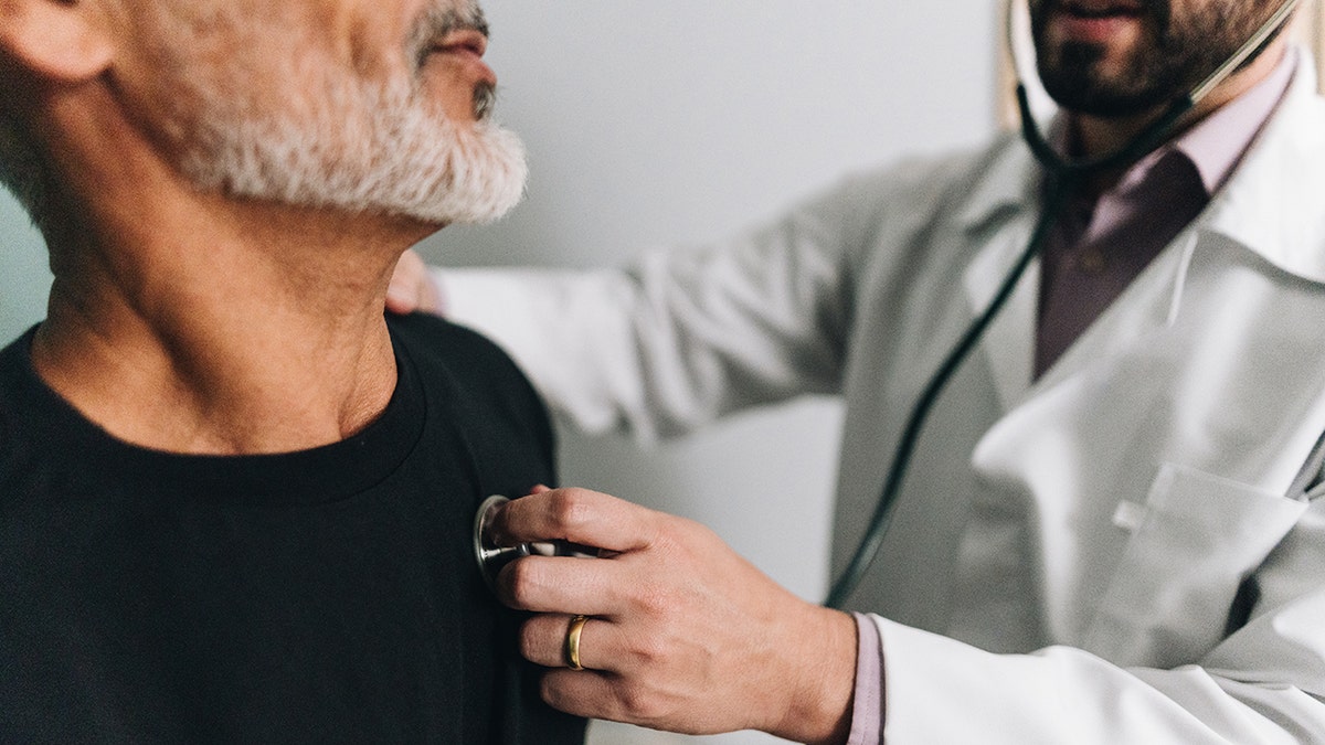 Male doctor seen close up listening to male doctors heart during medical exam.