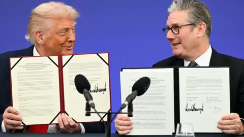 EPA Donald Trump and Sir Keir Starmer hold up signed copies of the Tech Prosperity Deal between the UK and US while sitting at a desk in front of a blue backdrop.
