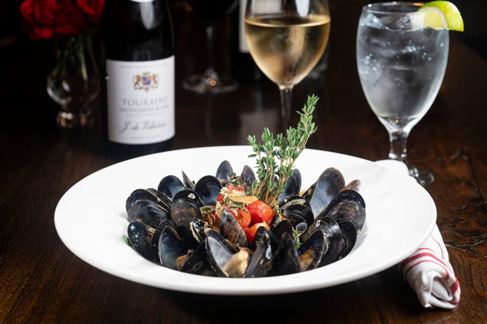 a bowl of mussels on a set table with a glass and bottle of wine