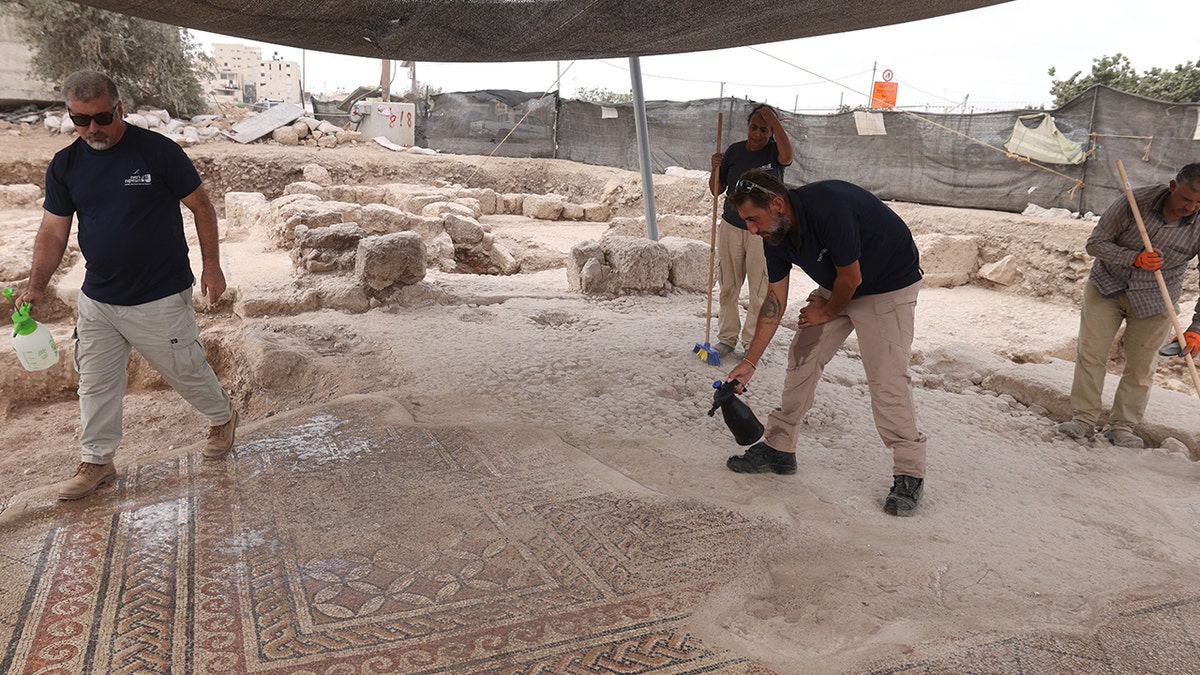 Several male archaeologists brushing dirt off mosaic