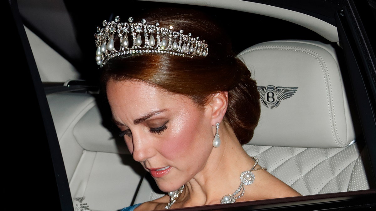 Kate Middleton looking down being driven in a car while wearing a tiara.
