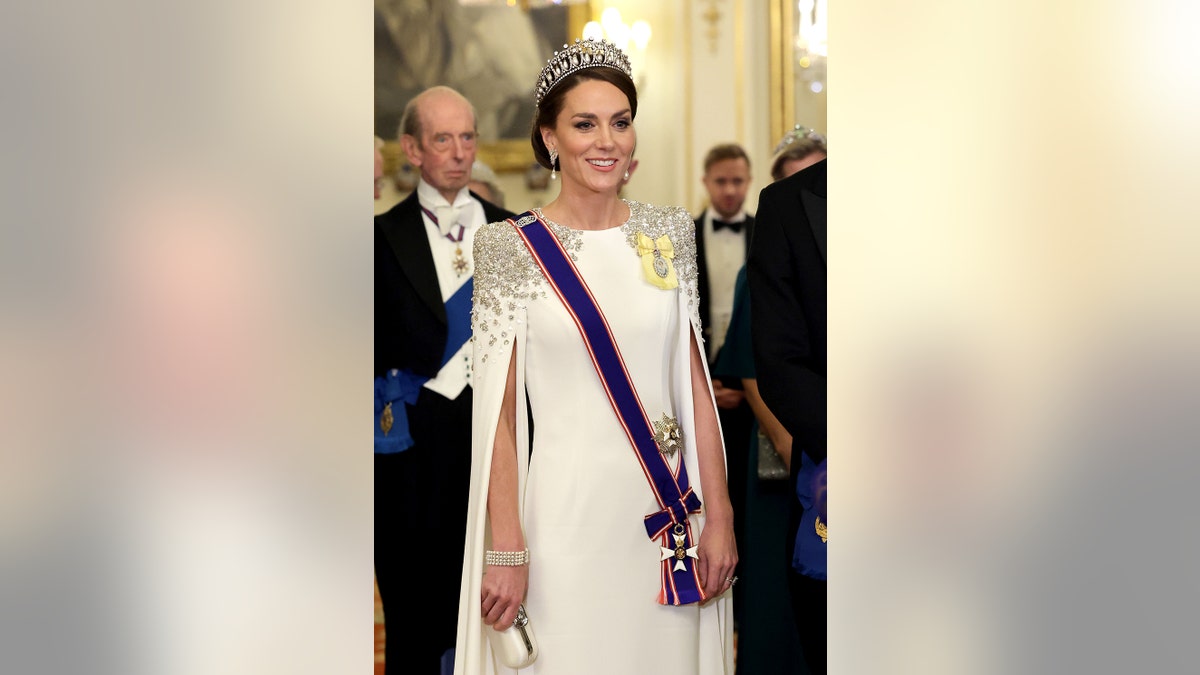 Kate Middleton in a white royal gown wearing a tiara and a blue sash.