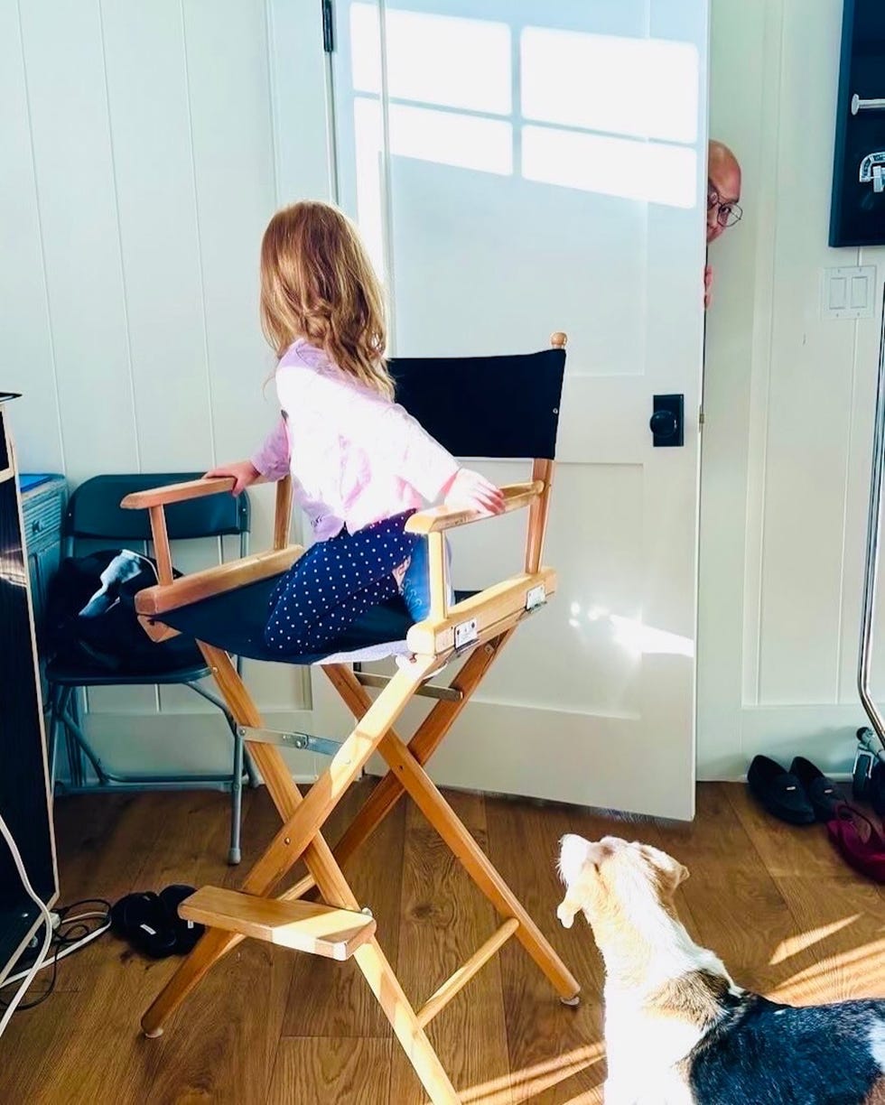 child sitting on a directors chair in an interior space with a dog nearby