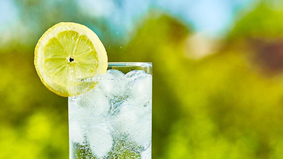 Sparkling water and lemon slice on glass with an ice, sunny day - narrow focus on middle of the glass