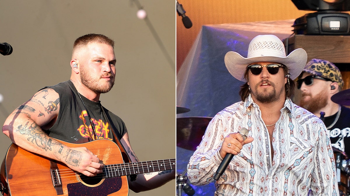 Zach Bryan strums a guitar while Gavin Adcock sings on stage.