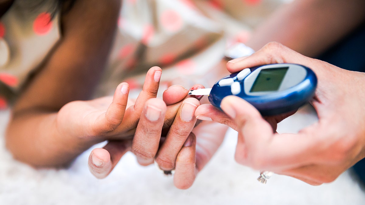 Mother is checking her daughters' diabetes by monitoring blood glucose.