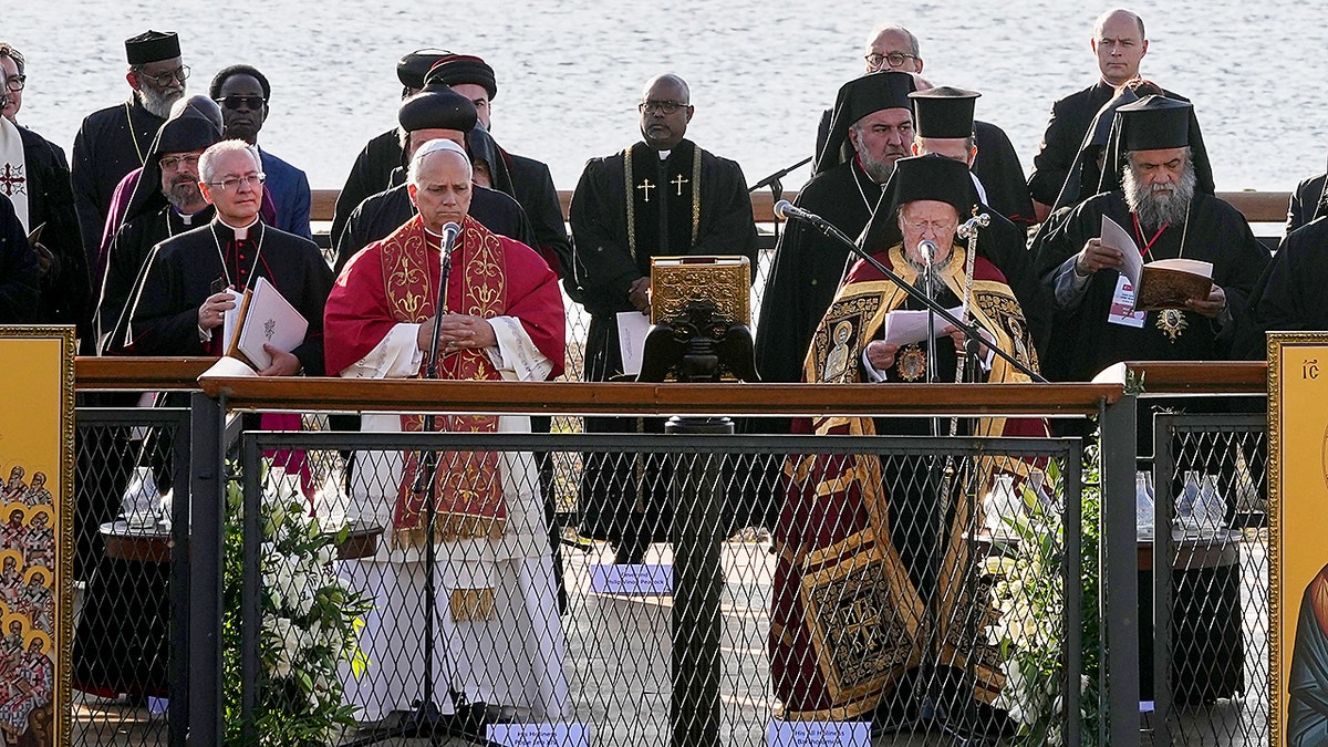 Religious leaders stand together on an outdoor platform leading a prayer service beside a waterfront.